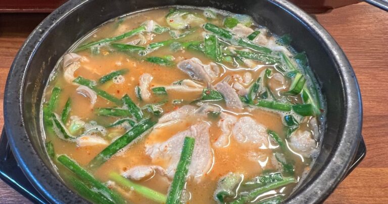 A steaming bowl of dwaeji gukbap served in a traditional ttukbaegi, with pork slices and chives in a light broth, Busan.